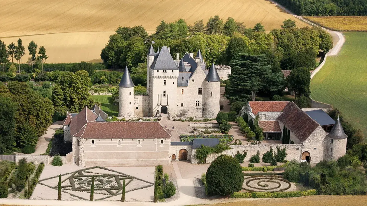 Vue aérienne du **château du Riveau**, un édifice médiéval entouré de jardins à la française et de champs dorés.