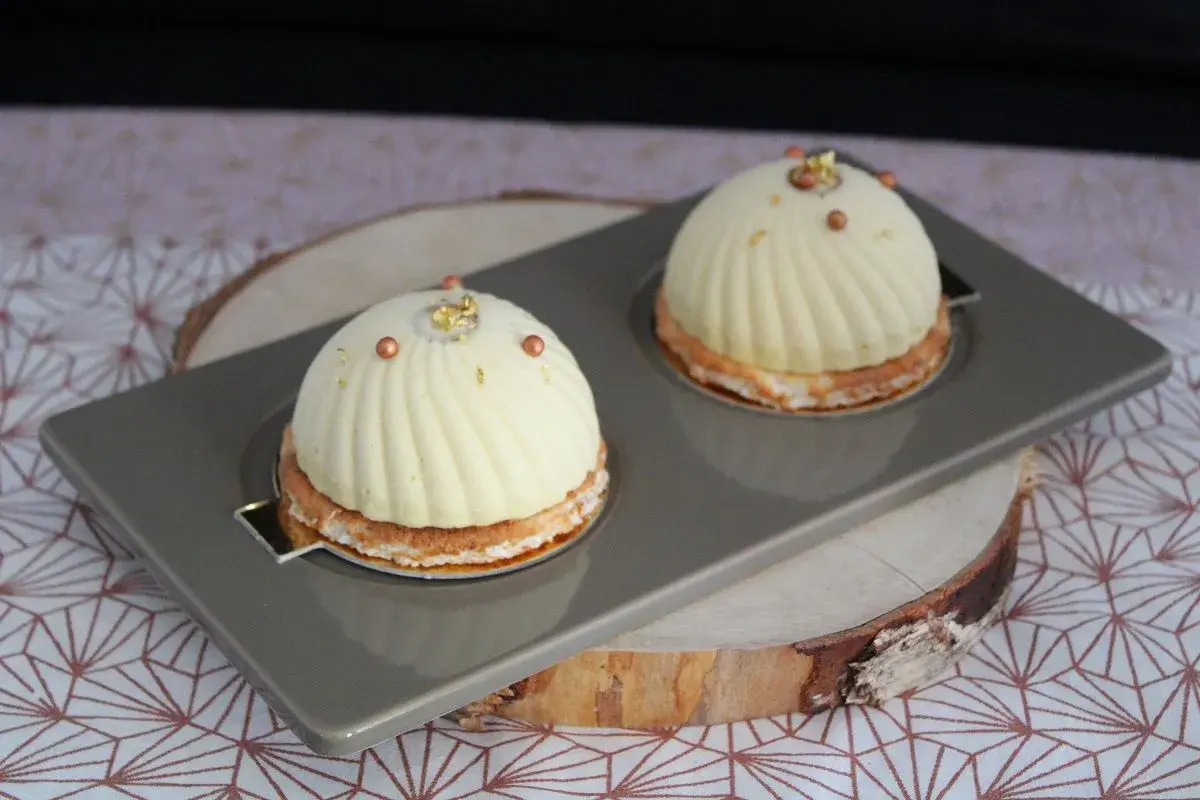 Deux dômes de dessert fruités, ornés de perles cuivrées et de feuilles d'or, reposent sur un plateau gris.