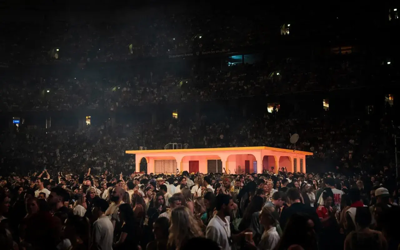 Stor publik på en konsert i Strawberry Arena. En rosa byggnad med gula detaljer står på scenen.