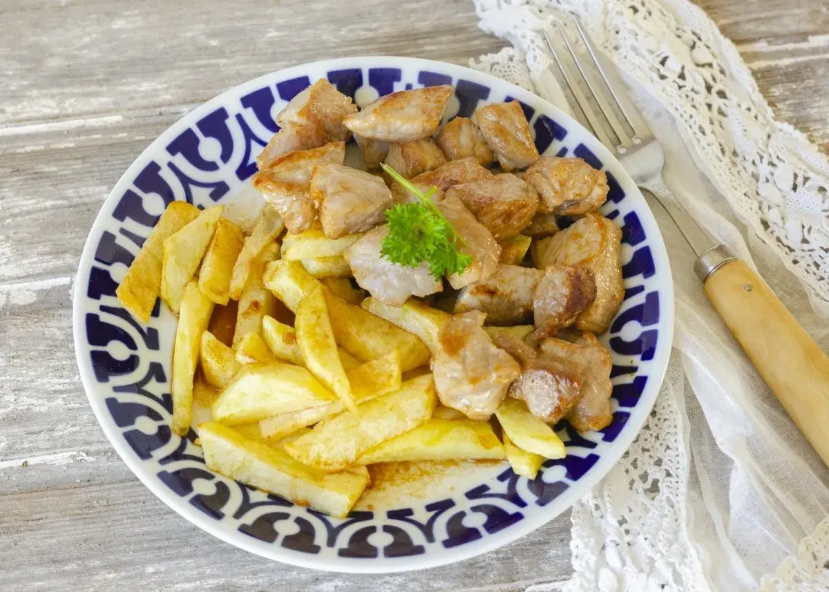 Un plato de raxo con patatas fritas, decorado con perejil fresco. Un clásico delicioso.