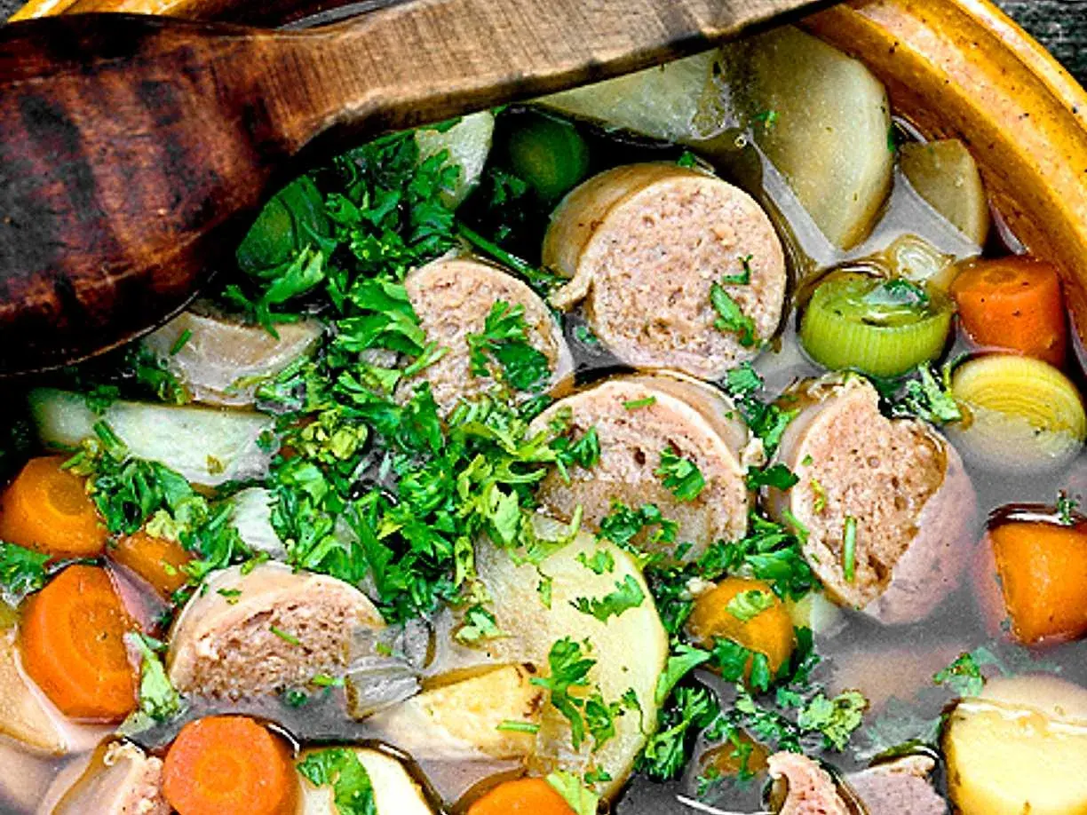 En närbild på en mustig korvgryta med potatis, morötter och purjolök, toppad med färsk persilja. Ett perfekt korvgryta recept för kalla dagar.