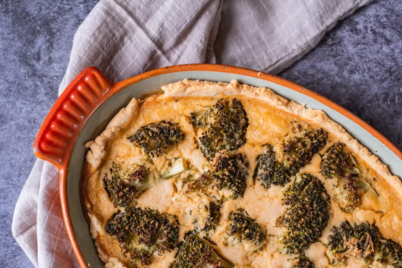 En gyllene ost och broccolipaj i en orange kantig form, redo att serveras.