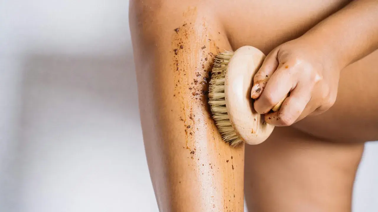 Mano che applica fango dimagrante con spazzola su gamba. Esfoliazione e benessere per la pelle.