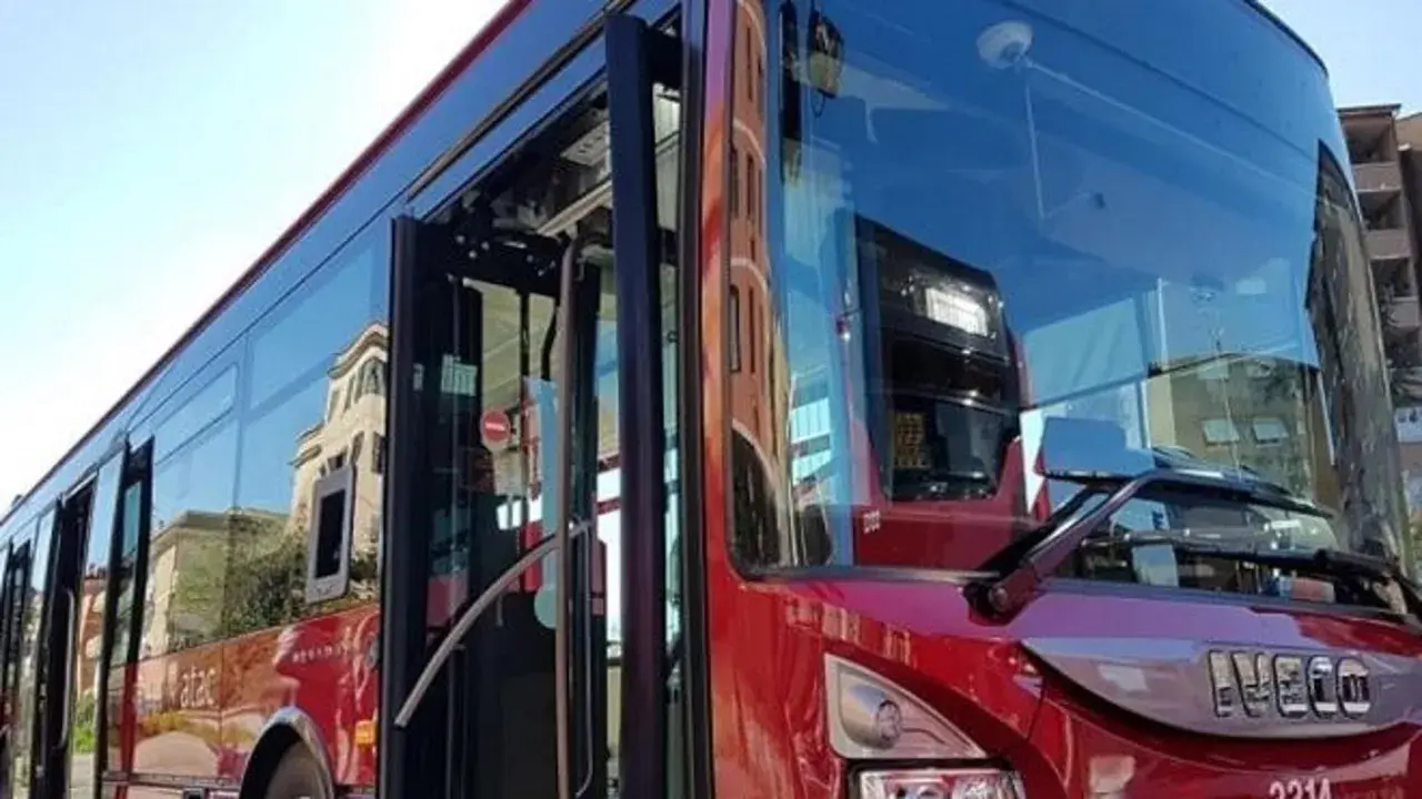 Autobus rosso con porte aperte, riflessi di palazzi sui vetri. Forse l'ultima metro della giornata, ma è un bus.
