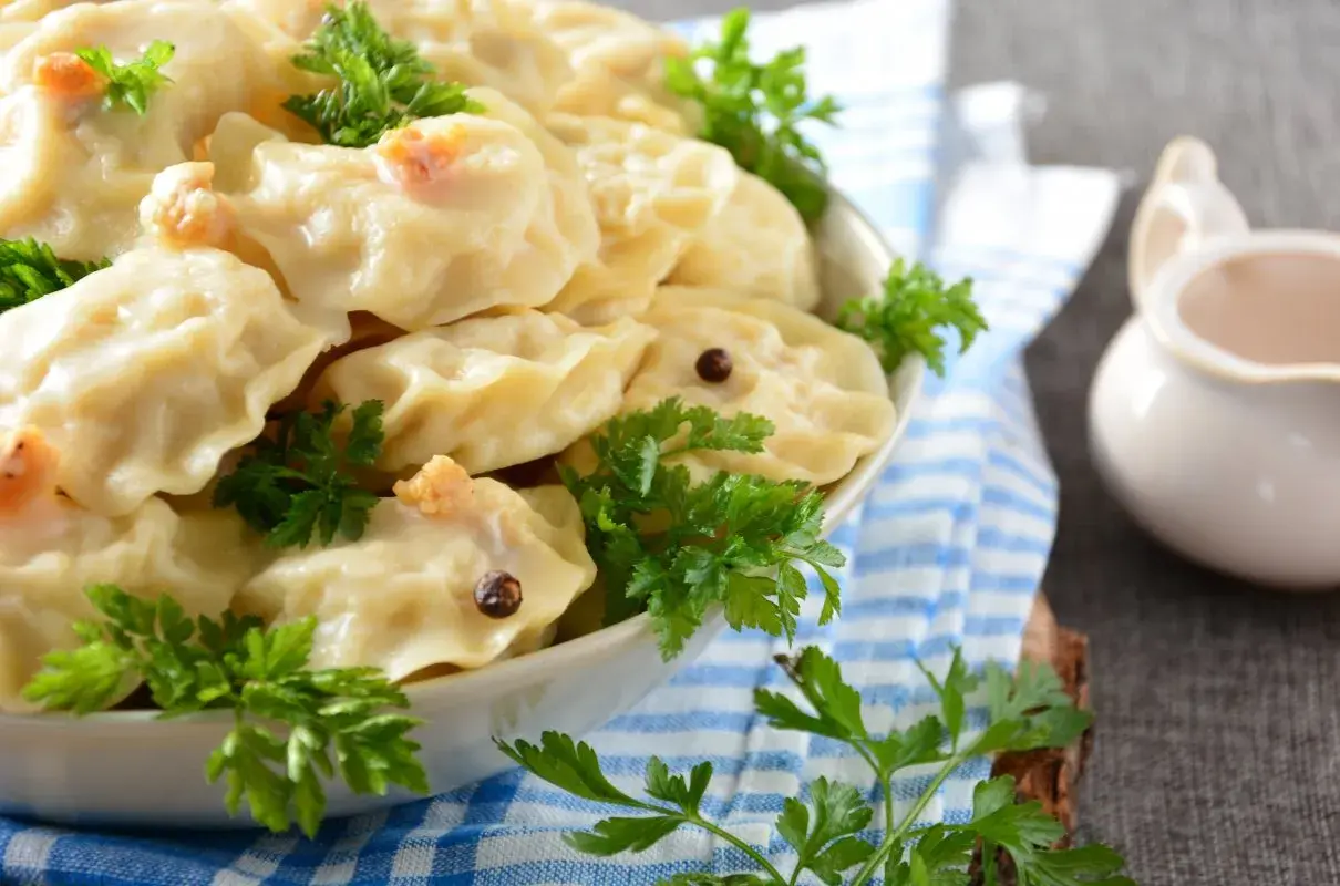 Pyszne pierogi z ziemniakami, udekorowane natką pietruszki i ziarnami pieprzu, czekają na talerzu.