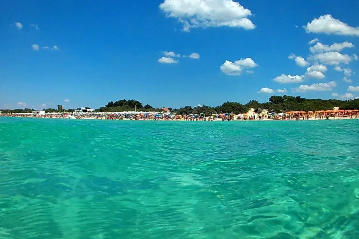 Acque cristalline e una spiaggia affollata a Porto Cesareo, con ombrelloni colorati e gente che si gode il sole. Lu specchia Porto Cesareo, un paradiso estivo.