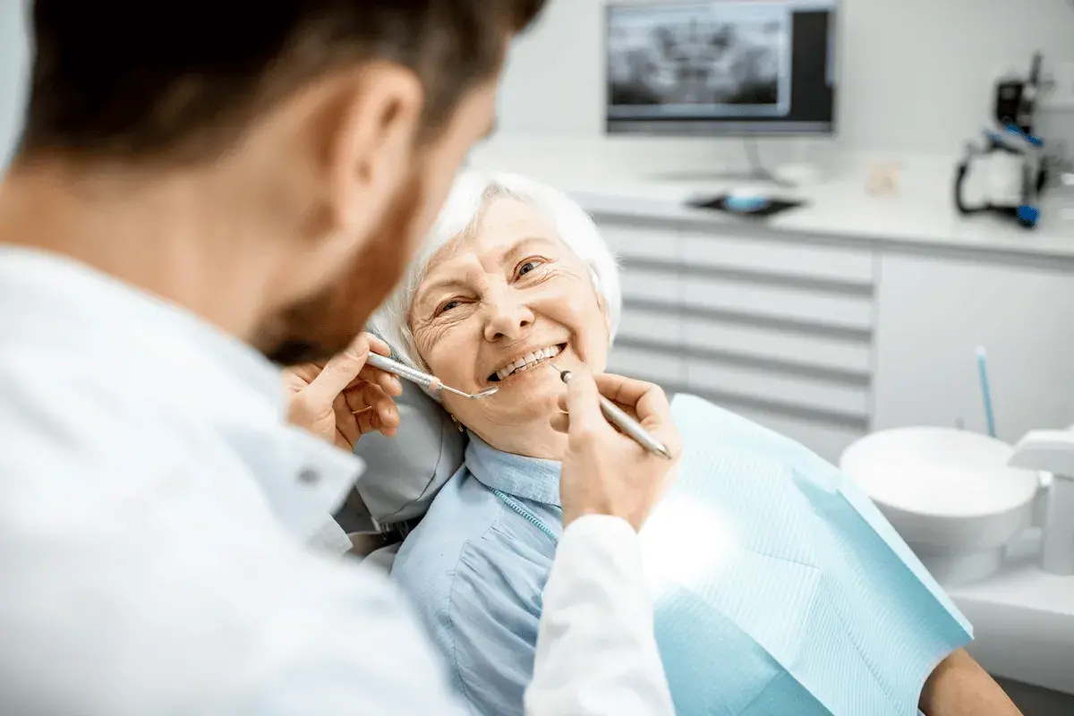 Un dentista esamina i denti di un'anziana sorridente, sottolineando l'importanza dell'igiene orale per gli anziani.