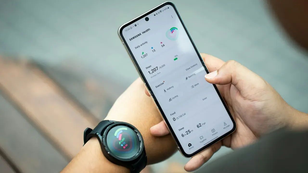 Ręka trzyma telefon Samsung z aplikacją Samsung Health, pokazującą kroki i aktywność. Zegarek na nadgarstku synchronizuje dane, pomagając jak znaleźć telefon Samsung.