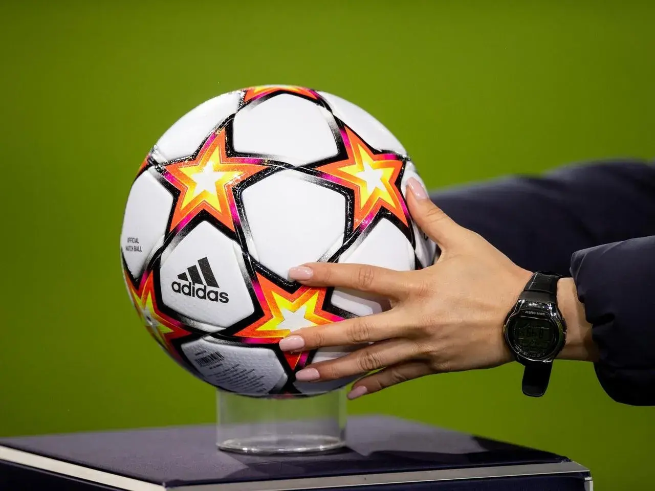 Dłoń z zegarkiem trzyma piłkę Adidas z gwiazdami, gotową do gry w ulubionym klubie piłkarskim na boisku.
