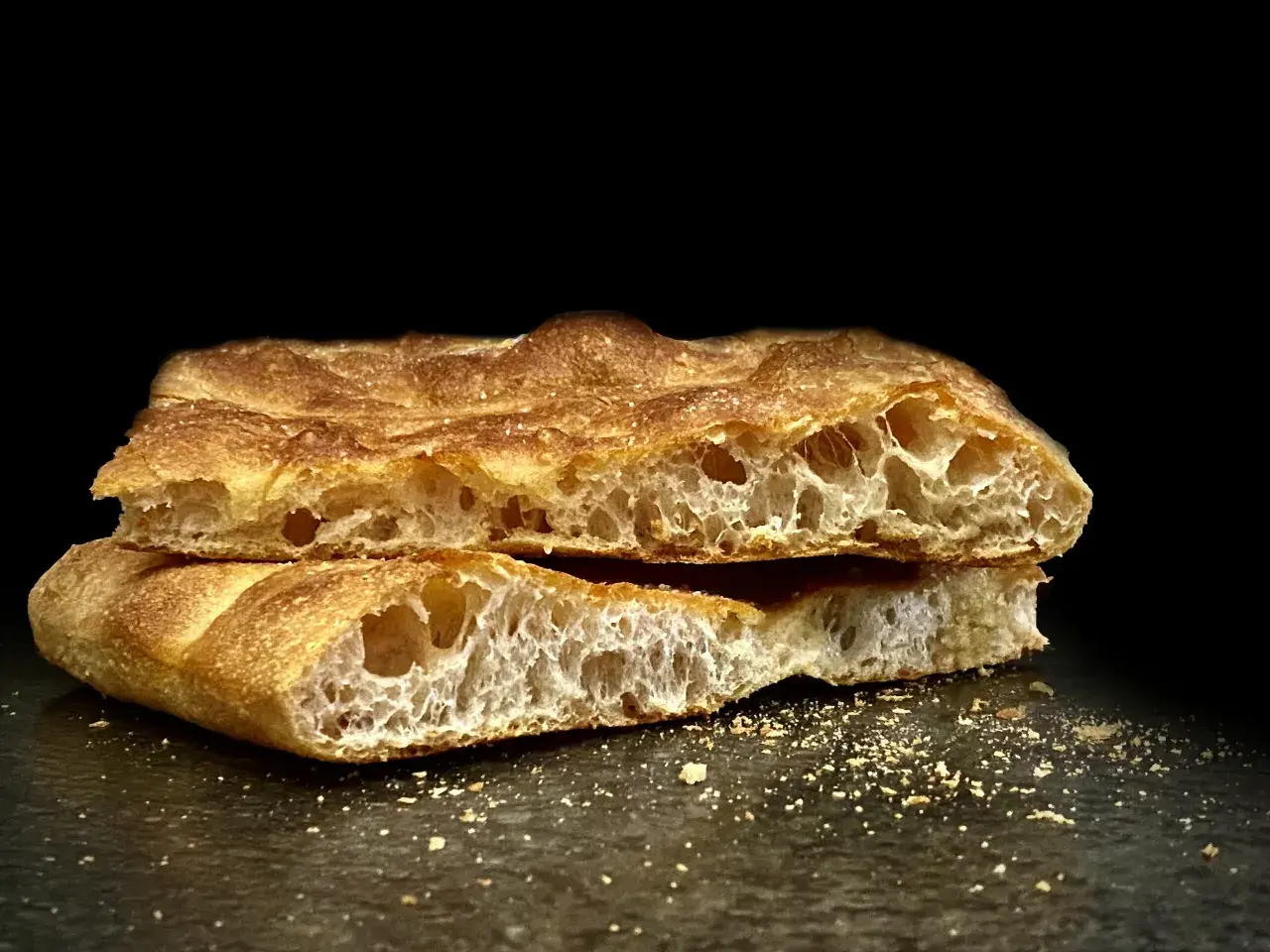 Schiacciata toscana dorata e fragrante, tagliata a metà, con alveolatura evidente e briciole sparse.
