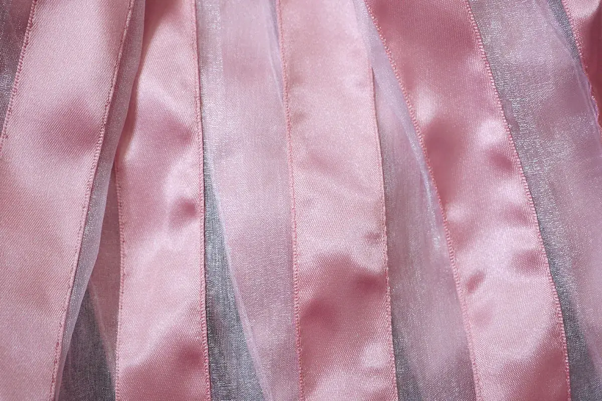 Bandes verticales de tissu brillant rose et argenté, créant un effet de texture doux et lumineux.