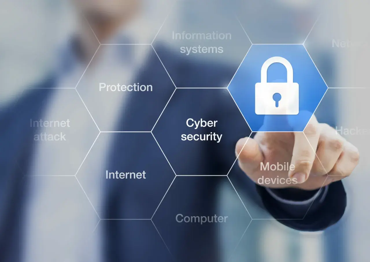 Palec dotyka ikony kłódki, symbolizującej cyberbezpieczeństwo. Wokół widnieją hasła: ochrona, internet, ataki, systemy informatyczne, urządzenia mobilne, komputery. To definicja cyberprzestępczości.