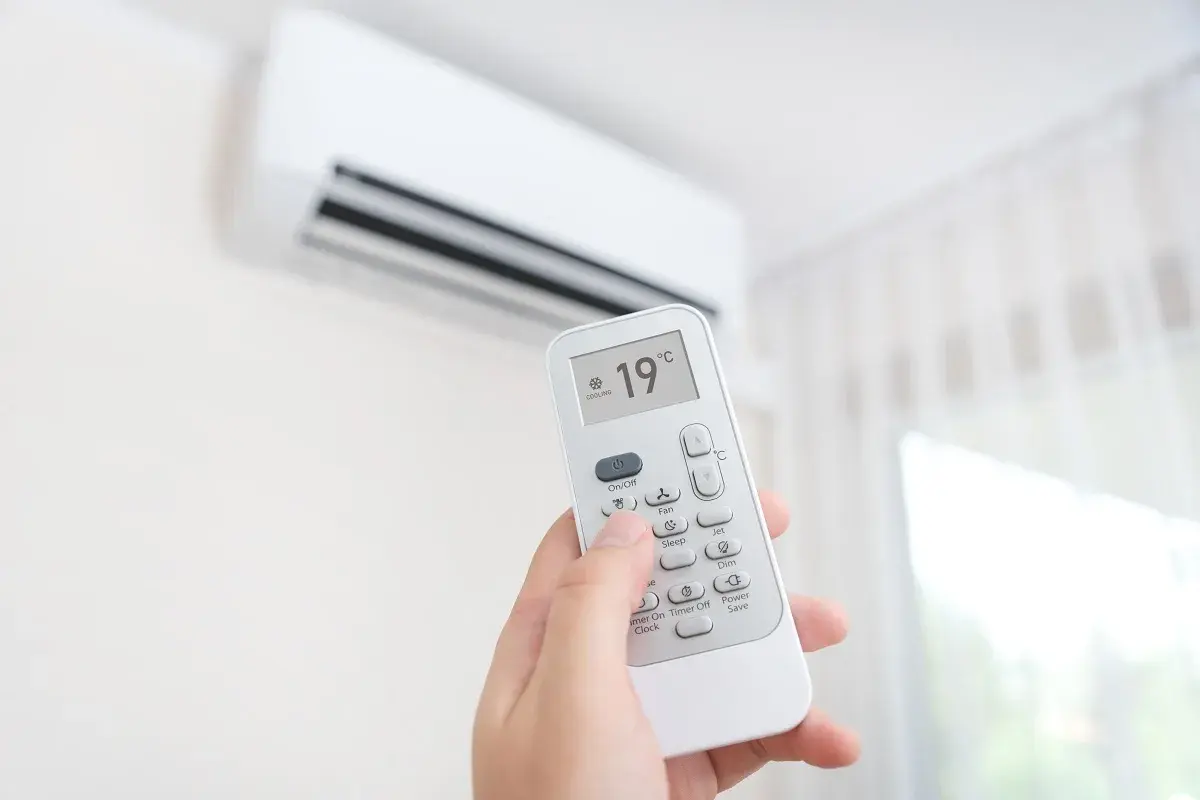 Mano sujetando control remoto de aire acondicionado, ajustando el símbolo frío a 19°C para un ambiente fresco.
