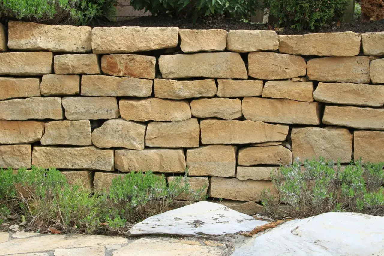 Eine rustikale Natursteinmauer bauen, die mit Lavendel und Steinen verziert ist.