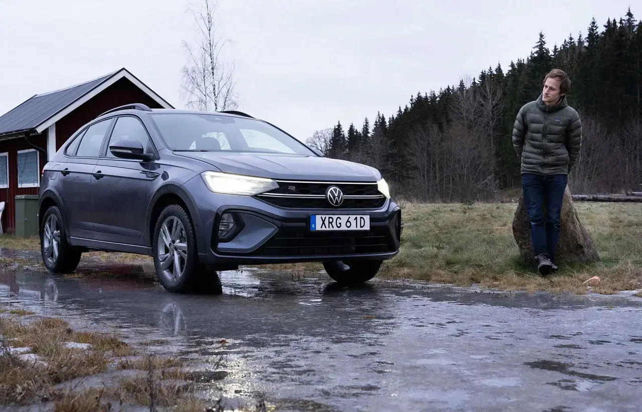 Grå VW Taigo står på en isig väg nära en röd stuga. En man står lutad mot en sten i bakgrunden.