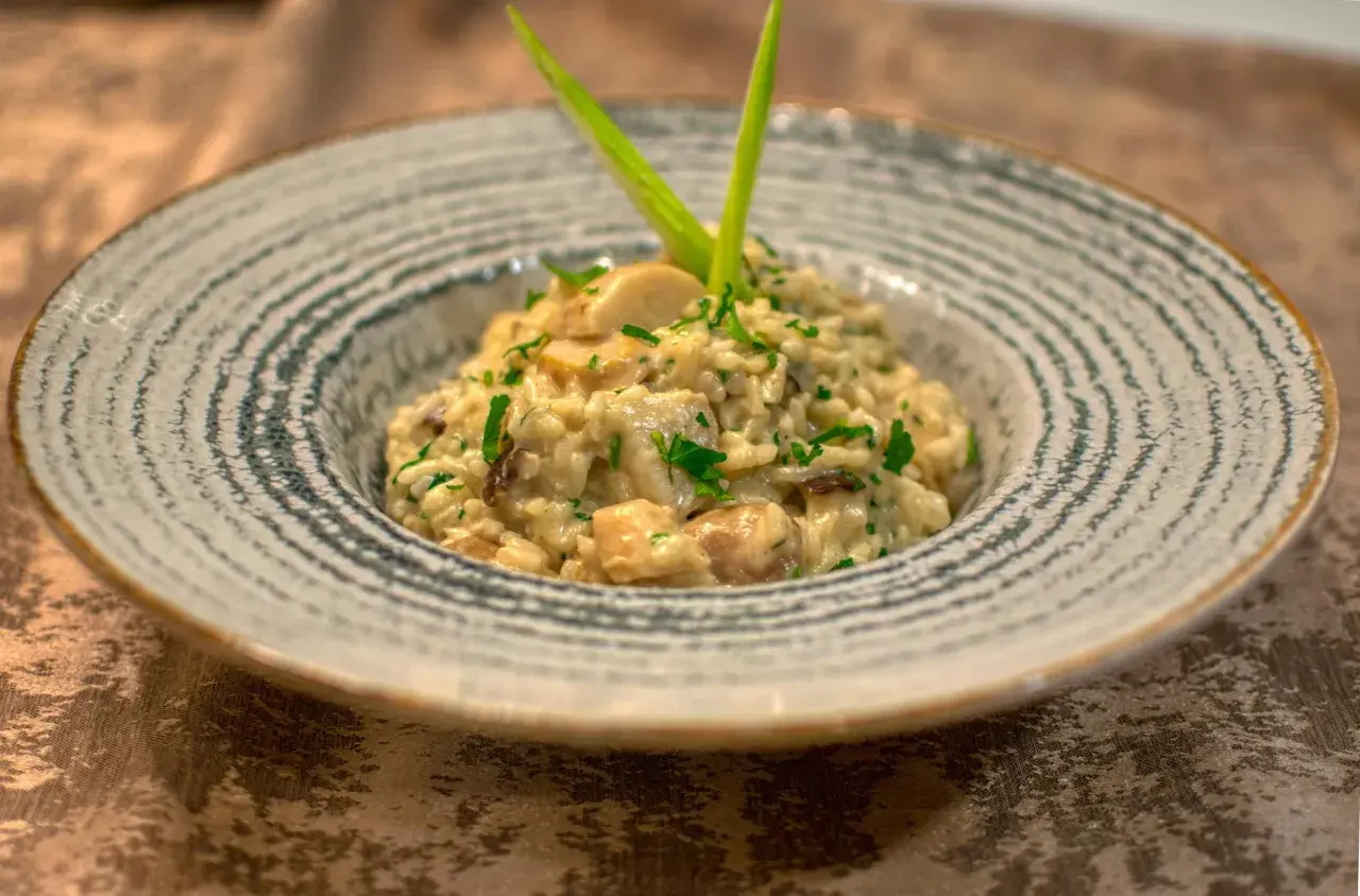 Kremowe risotto ze szparagami i grzybami, udekorowane zieloną cebulką i natką pietruszki, podane w ozdobnej misce.