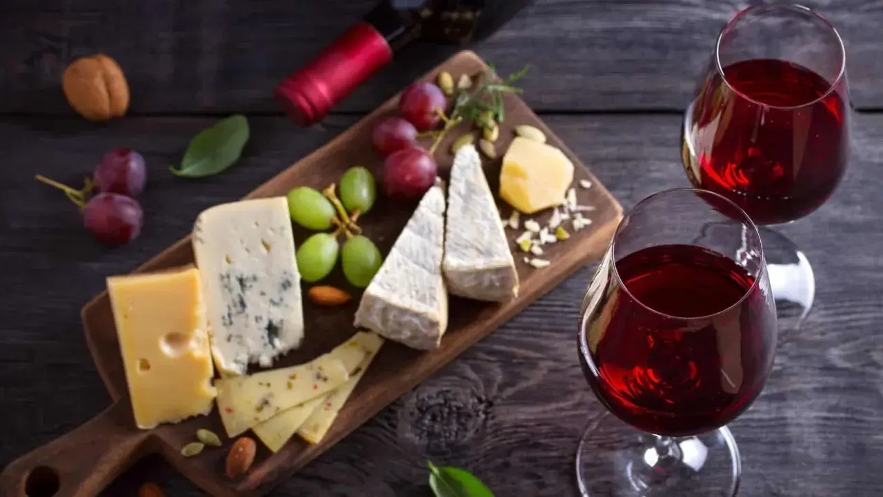 Un tagliere di formaggi misti, uva e frutta secca, perfetto per i rosso di Montalcino abbinamenti. Due calici di vino rosso completano la scena.