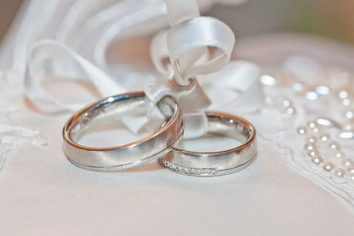 Anillos de oro blanco atados con cinta, uno con diamantes. El oro blanco se pone feo con el tiempo, pero el amor perdura.