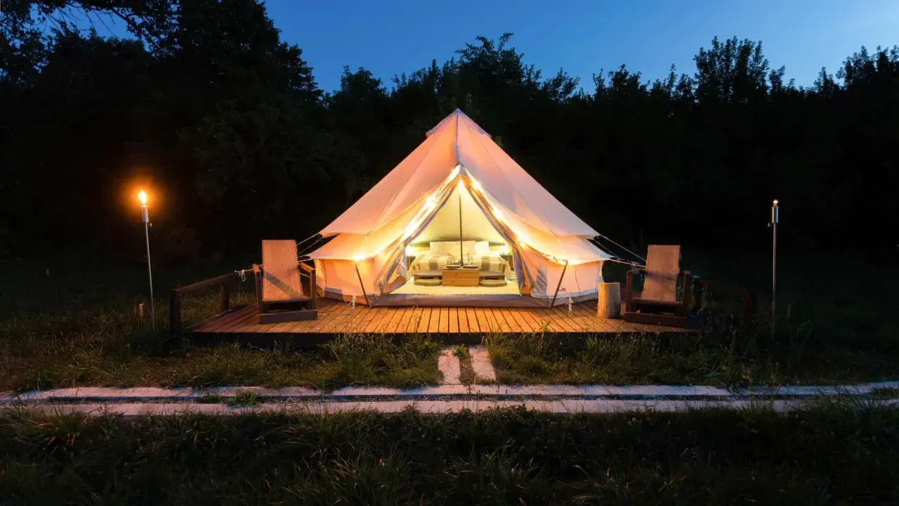 Tienda iluminada para camping Portugal, ideal para familias con niños. Dos sillas de madera esperan en la terraza.