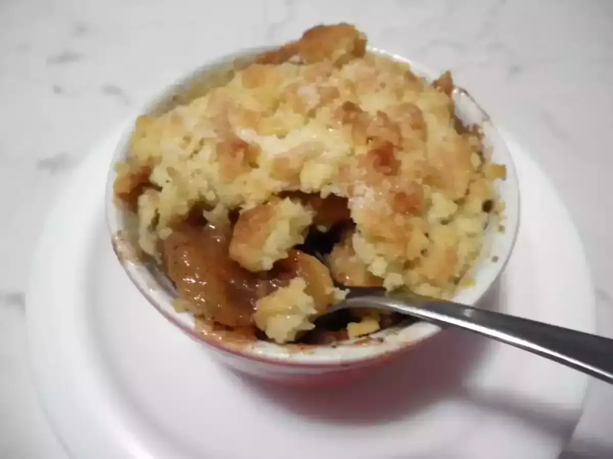 Un delizioso crumble di mele appena sfornato, con la crosta dorata e il ripieno succoso. Una forchetta è immersa nel dolce.