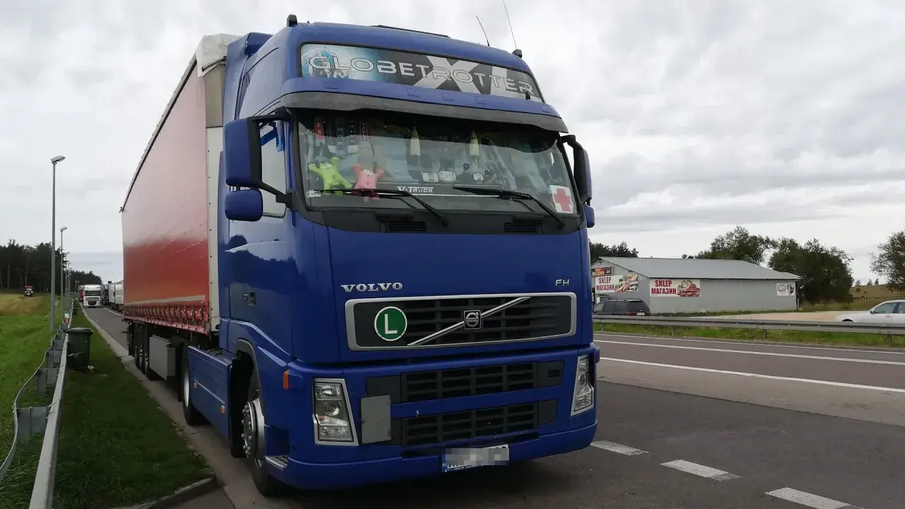 Niebieski Volvo FH Globetrotter z naczepą, zaparkowany przy drodze. W tle sklep i inne ciężarówki. Zakazy dla ciężarówek 40ton.