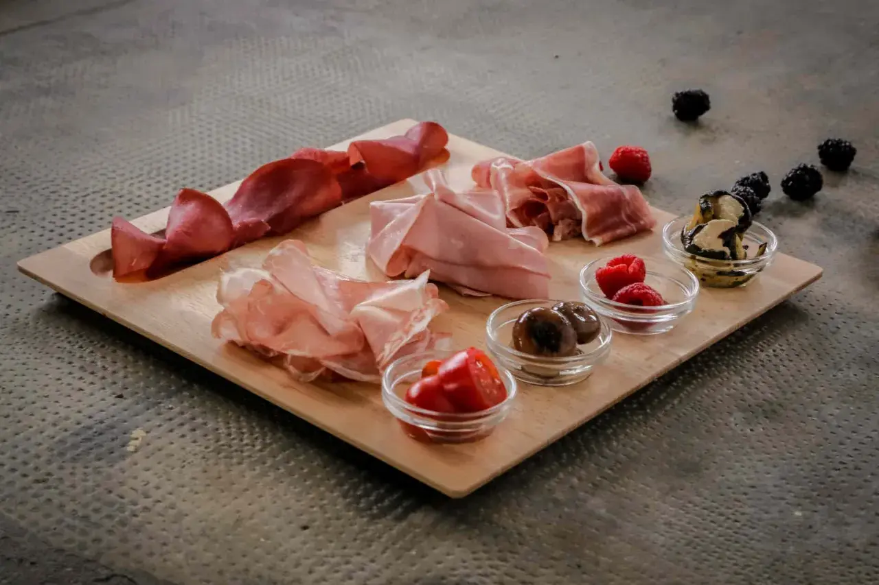 Un invitante tagliere di antipasti con salumi, olive, pomodorini e frutti di bosco, pronto per essere gustato.
