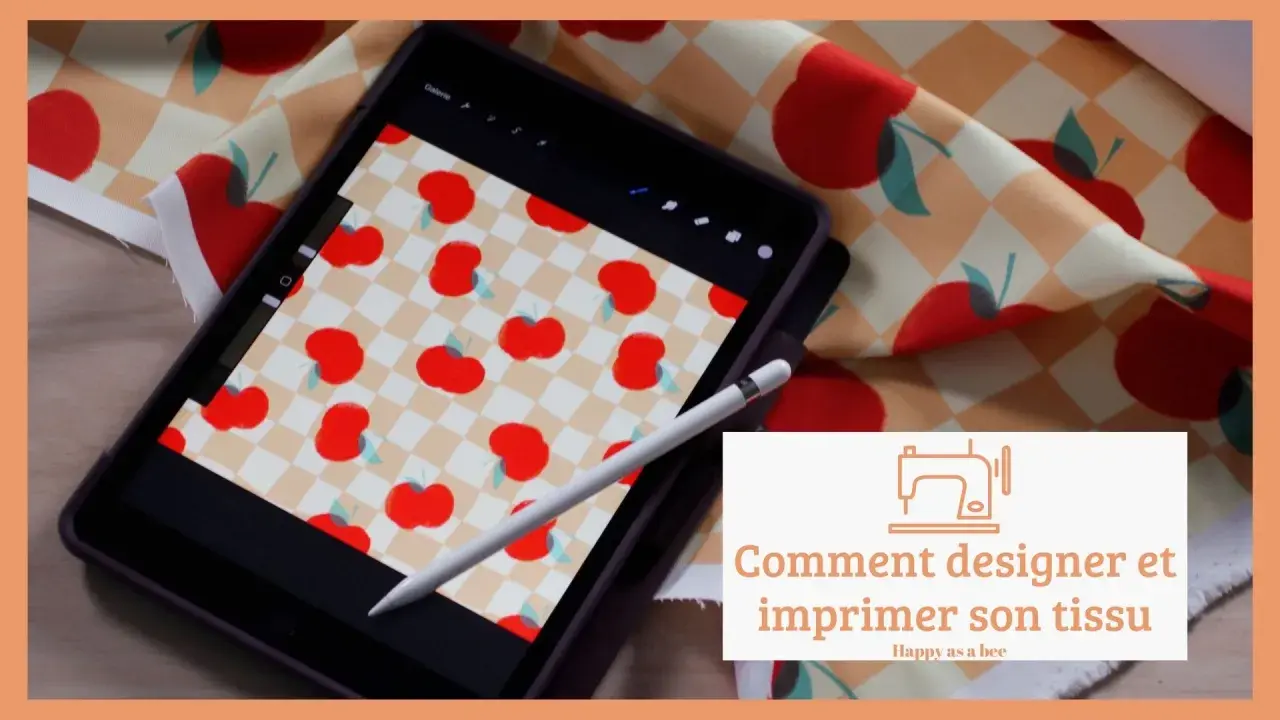 Un dessin sur tissu motif de pommes rouges sur fond à carreaux, visible sur une tablette et un échantillon de tissu.