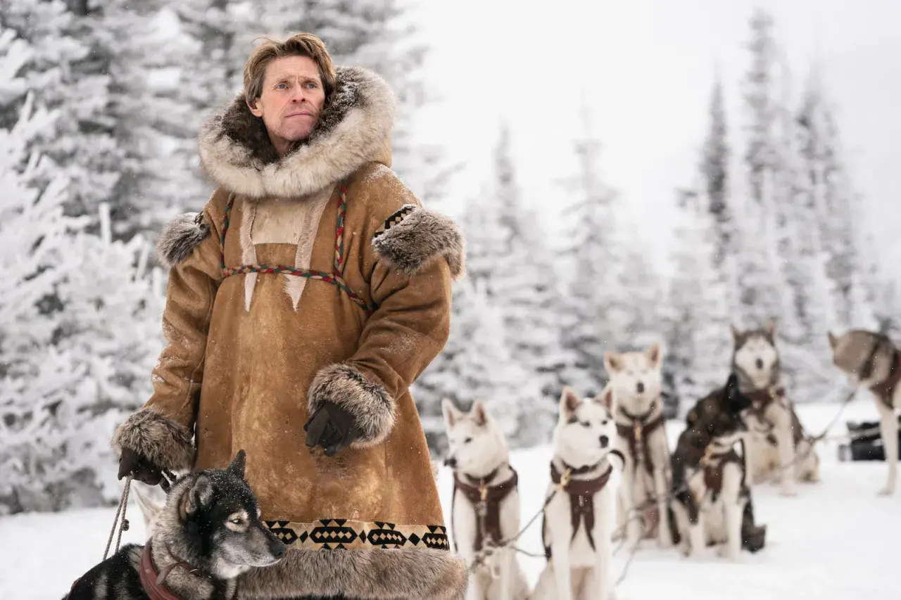 Man i pälsrock med hundspann i snöig skog. Scen från en togo film.