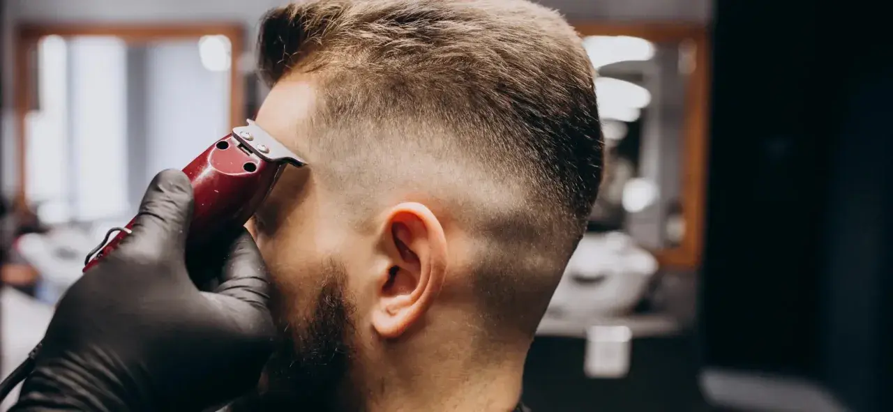 Barbero con guantes negros crea un corte de pelo **low fade** a un hombre con una máquina.