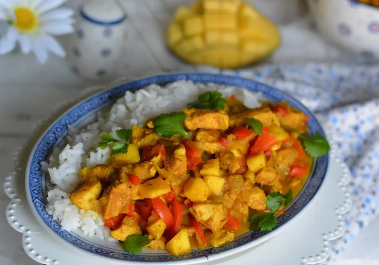 Pyszny kurczak z mango po tajsku, podany z ryżem. Aromatyczne kawałki kurczaka, słodkie mango i papryka w złocistym sosie curry.