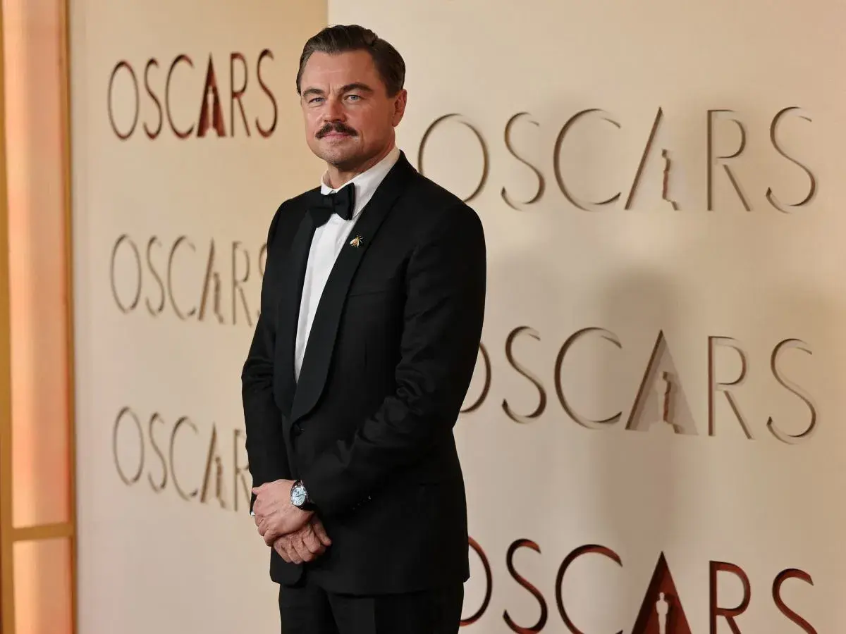 Leonardo DiCaprio w eleganckim smokingu pozuje na tle ścianki z napisem "OSCARS".
