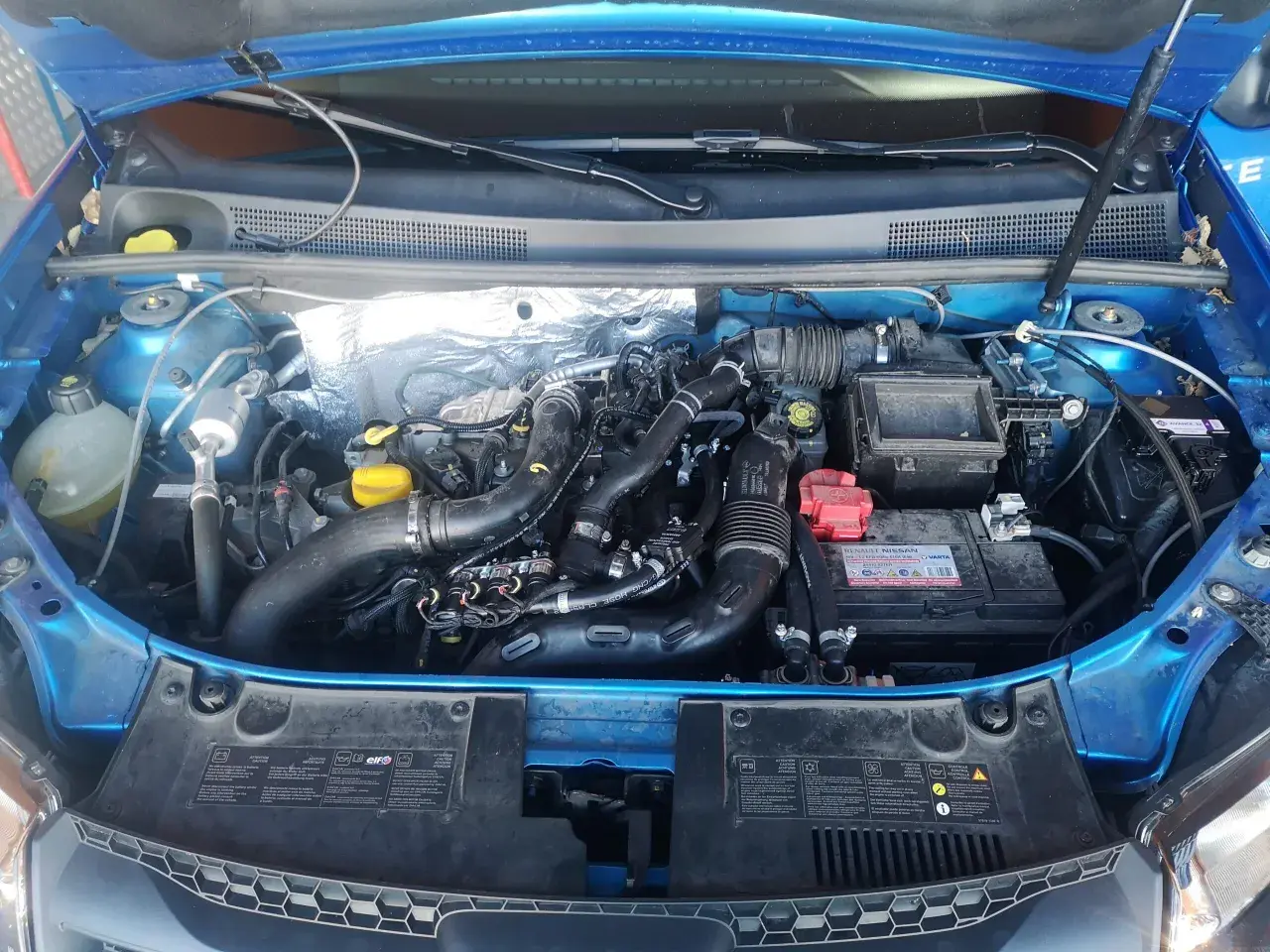 Motor de Dacia Sandero GLP con mangueras de gas y batería. Posibles problemas de instalación o mantenimiento.