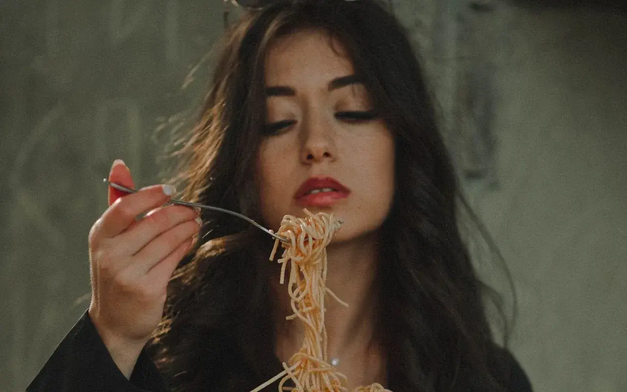 Włoska uroda w pełnej krasie. Kobieta z ciemnymi włosami i czerwoną szminką na ustach je spaghetti.