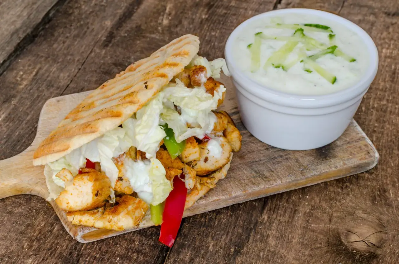 Gyros z kurczakiem, warzywami i sosem tzatziki na desce drewnianej.