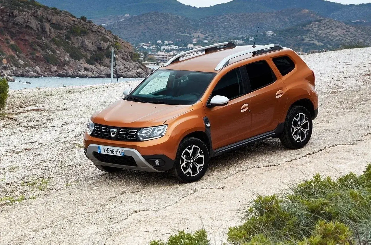 Pomarańczowy Dacia Duster na drodze szutrowej. Wiele osób szuka dacia duster opinie forum, by dowiedzieć się więcej o tym modelu.