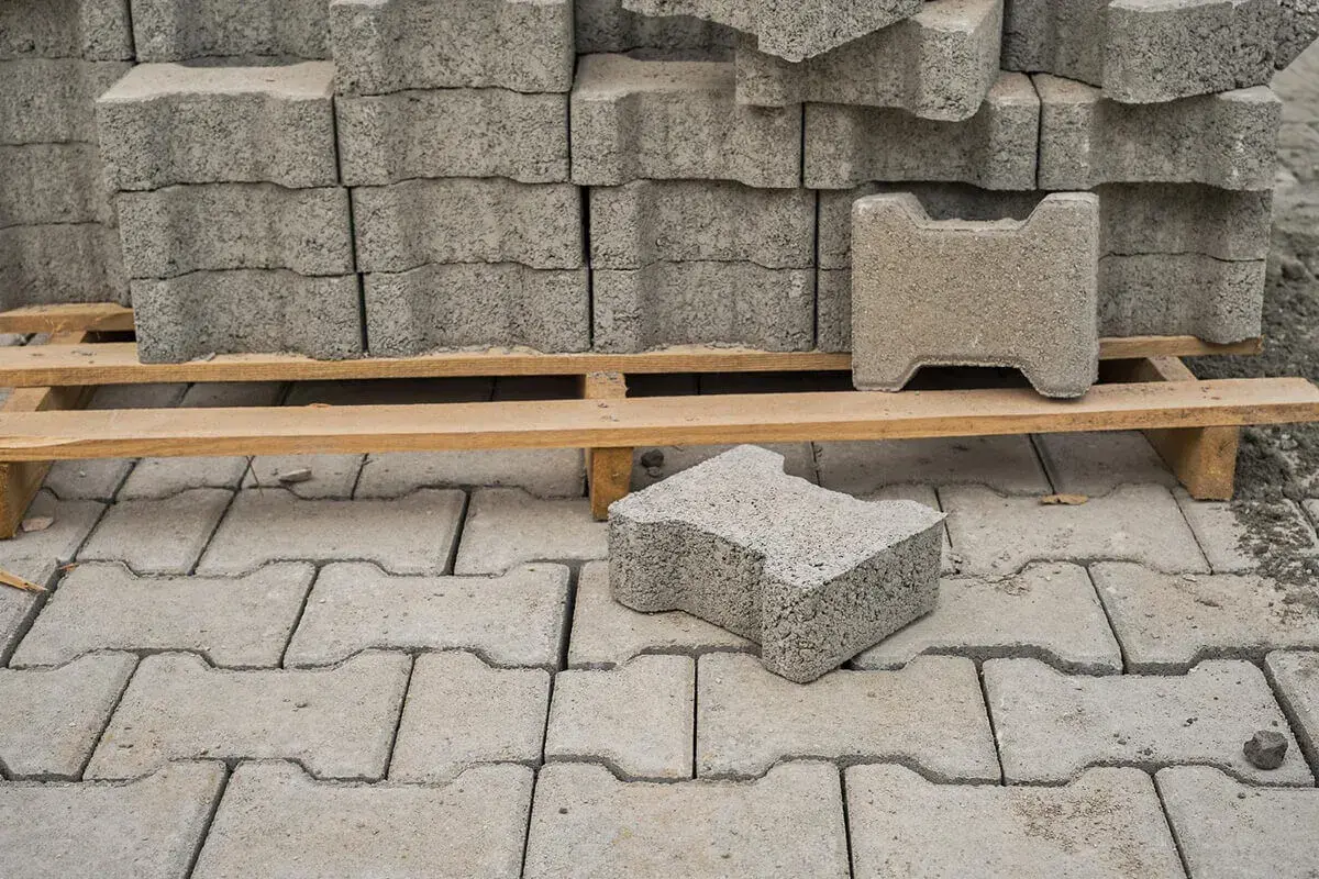 Stos kostki brukowej na palecie i pojedyncze elementy na ułożonej nawierzchni.