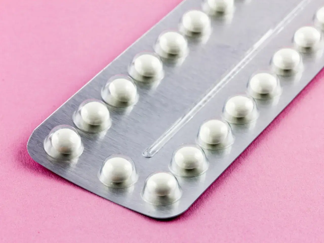 Eine Blisterpackung mit weißen Pillen auf rosa Untergrund. Die Pillen sind bereit, um sie durchzunehmen.