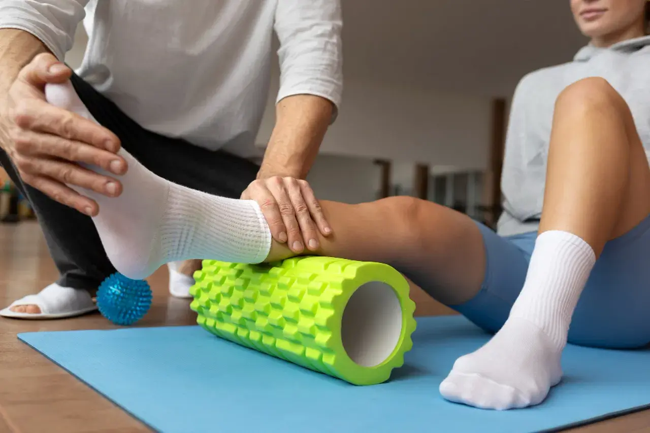 Fizjoterapeuta pomaga sportowcowi w automasażu łydki wałkiem, co jest kluczowe w klinicznej medycynie sportowej.