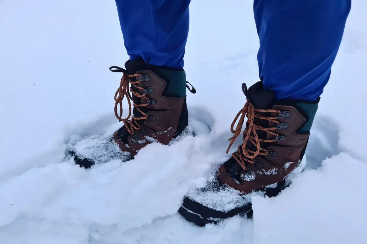 A person wearing blue pants and brown hiking boots stands in deep snow. These boots seem to be performing well, raising the question: can hiking boots be used as snow boots?