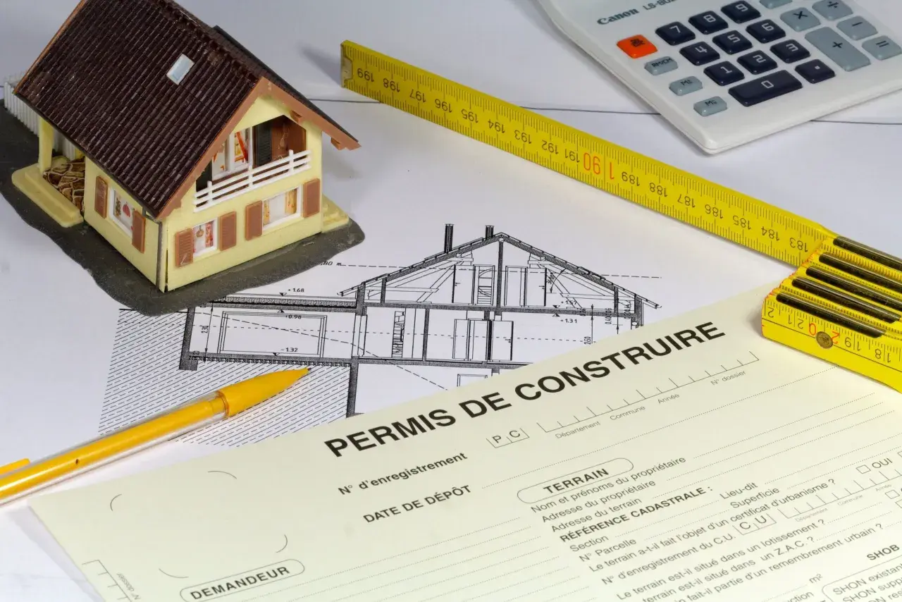 Maquette de maison, plans, mètre, calculatrice et formulaire "Permis de construire". La question : peut-on commencer les travaux pendant le recours des tiers ?