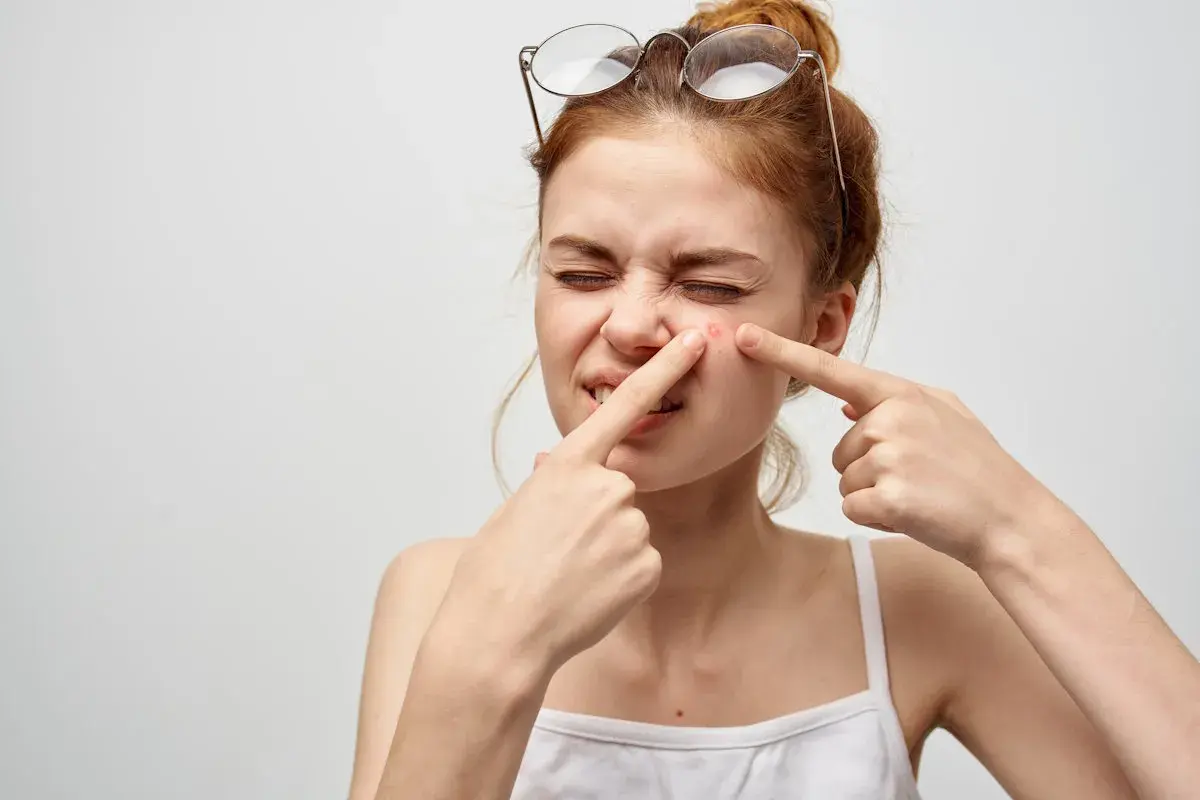 Ragazza con occhiali in testa che si tocca un brufolo, un fastidioso punto nero che si riforma sempre.