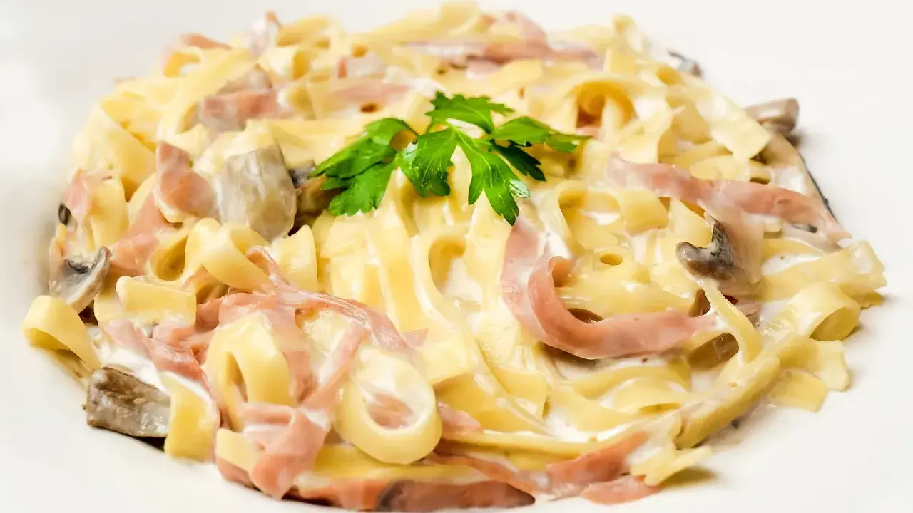 Pasta carbonara con setas y bacon, cremosa y deliciosa, coronada con perejil fresco.