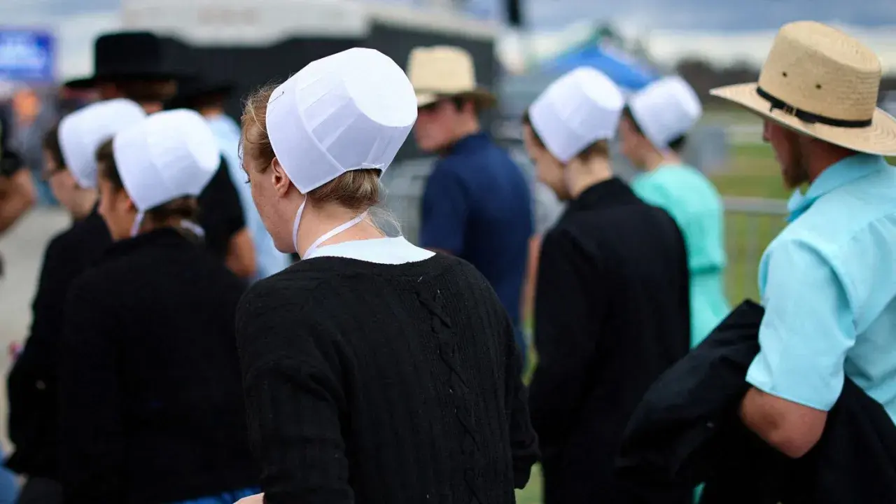 Människor i traditionella kläder, som påminner om amish i Sverige, med vita hättor och hattar.