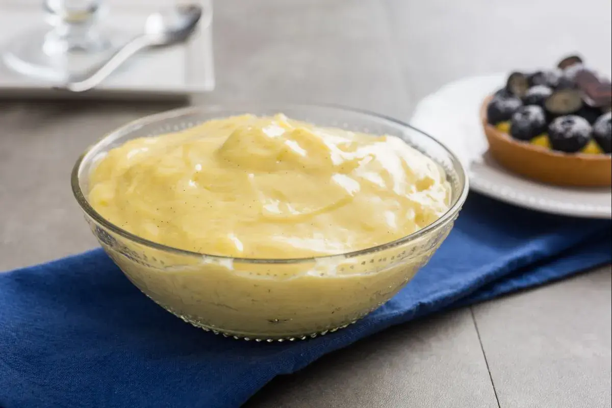 Cremige, vanilleschotenhaltige Crema Pasticcera in einer Glasschüssel, daneben ein Blaubeer-Törtchen.