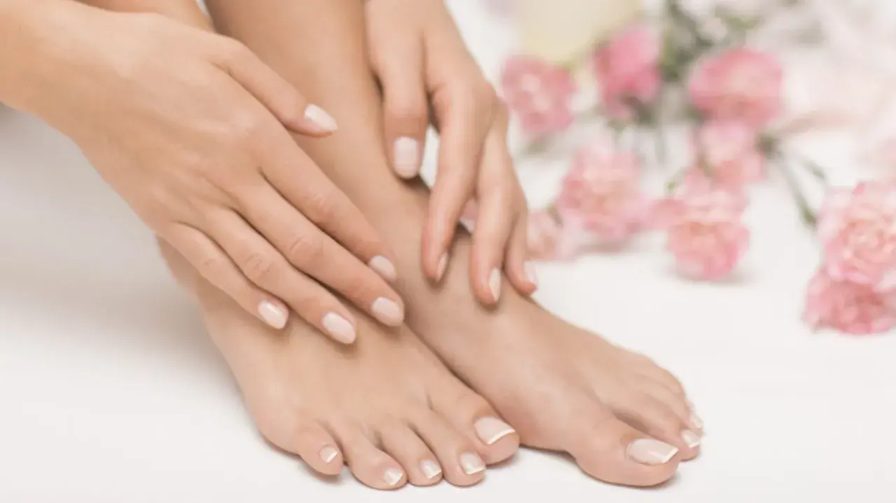 Pieds et mains soignés avec une french pedicure parfaite, entourés de fleurs roses délicates.