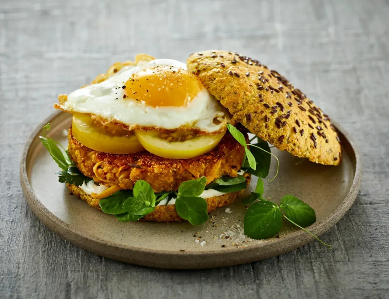Herzhafter Burger mit einem Spiegelei-Rezept-Topping, Tomatenscheiben, Salat und einer würzigen Pattie auf einem Körnerbrötchen.