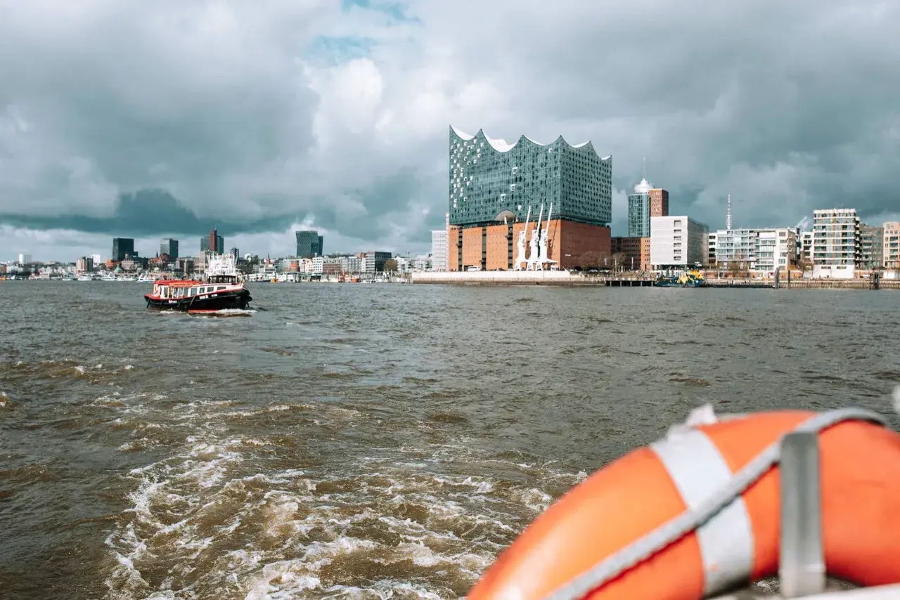 Blick vom Wasser auf Hamburgs Elbphilharmonie und die Skyline. Eine kleine Barkasse fährt vorbei. Welche Hafenrundfahrt in Hamburg ist die beste?