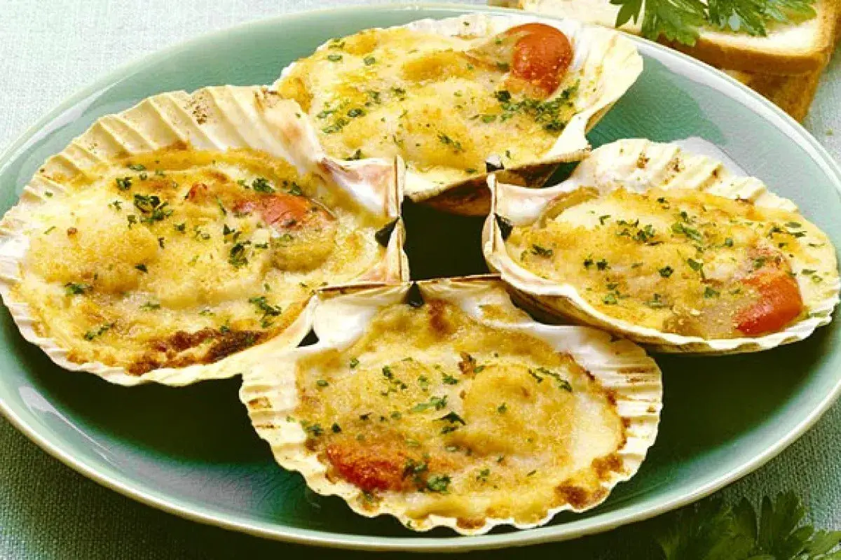 Quattro capesante gratinate, un delizioso antipasto di pesce, servite in conchiglia con erbe aromatiche.