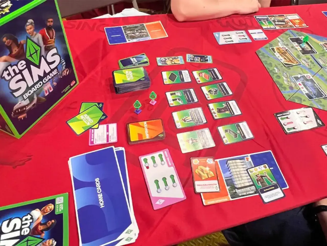 Gra planszowa The Sims w akcji. Widać pudełko, karty akcji, karty domów i planszę. Premiera The Sims Board Game zapowiada się świetnie!