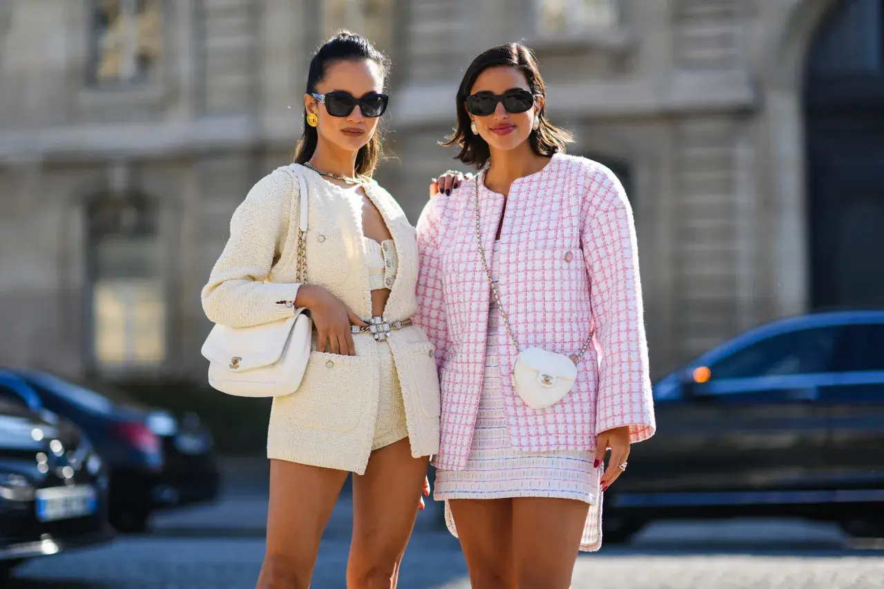 Dos mujeres lucen conjuntos de tweed, uno blanco y otro rosa, encarnando la moda preppy con bolsos a juego y gafas de sol.
